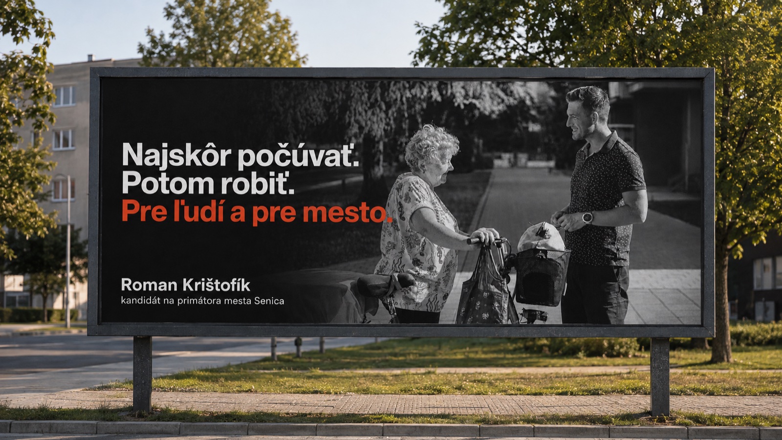 Billboard v uliciach Senice — čiernobiela fotografia Romana Krištofíka v rozhovore so staršou pani, nadpis Najskôr počúvať. Potom robiť. Pre ľudí a pre mesto.